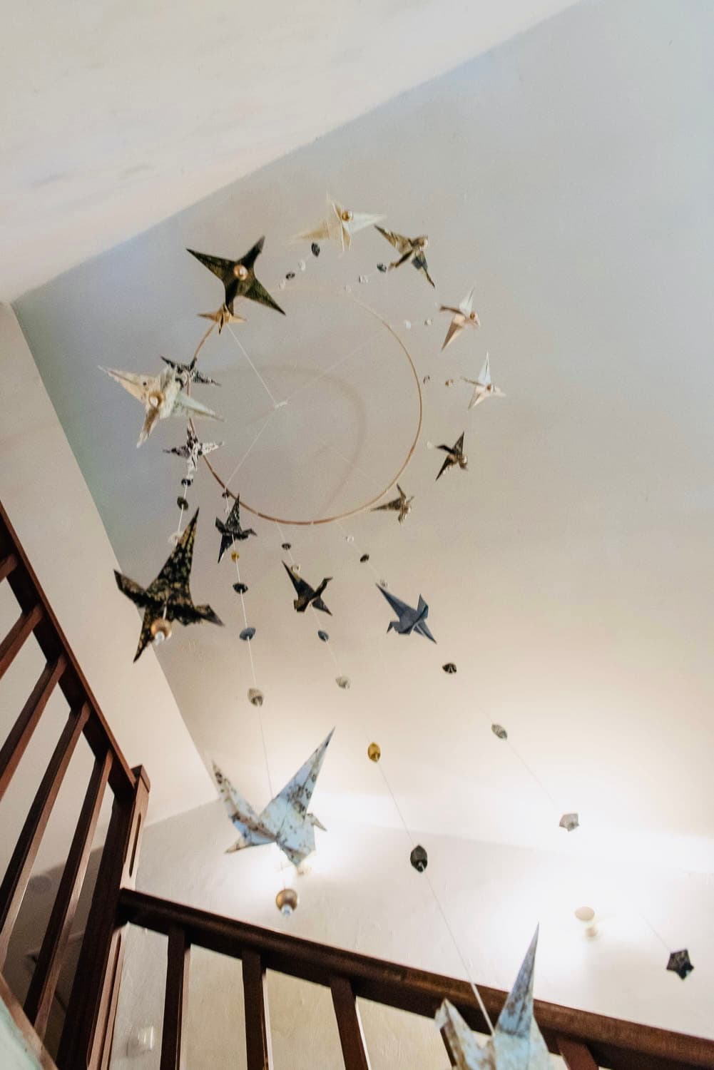 Spirale de grues et étoiles en origami washi, suspendue au plafond d'une cage d'escalier.