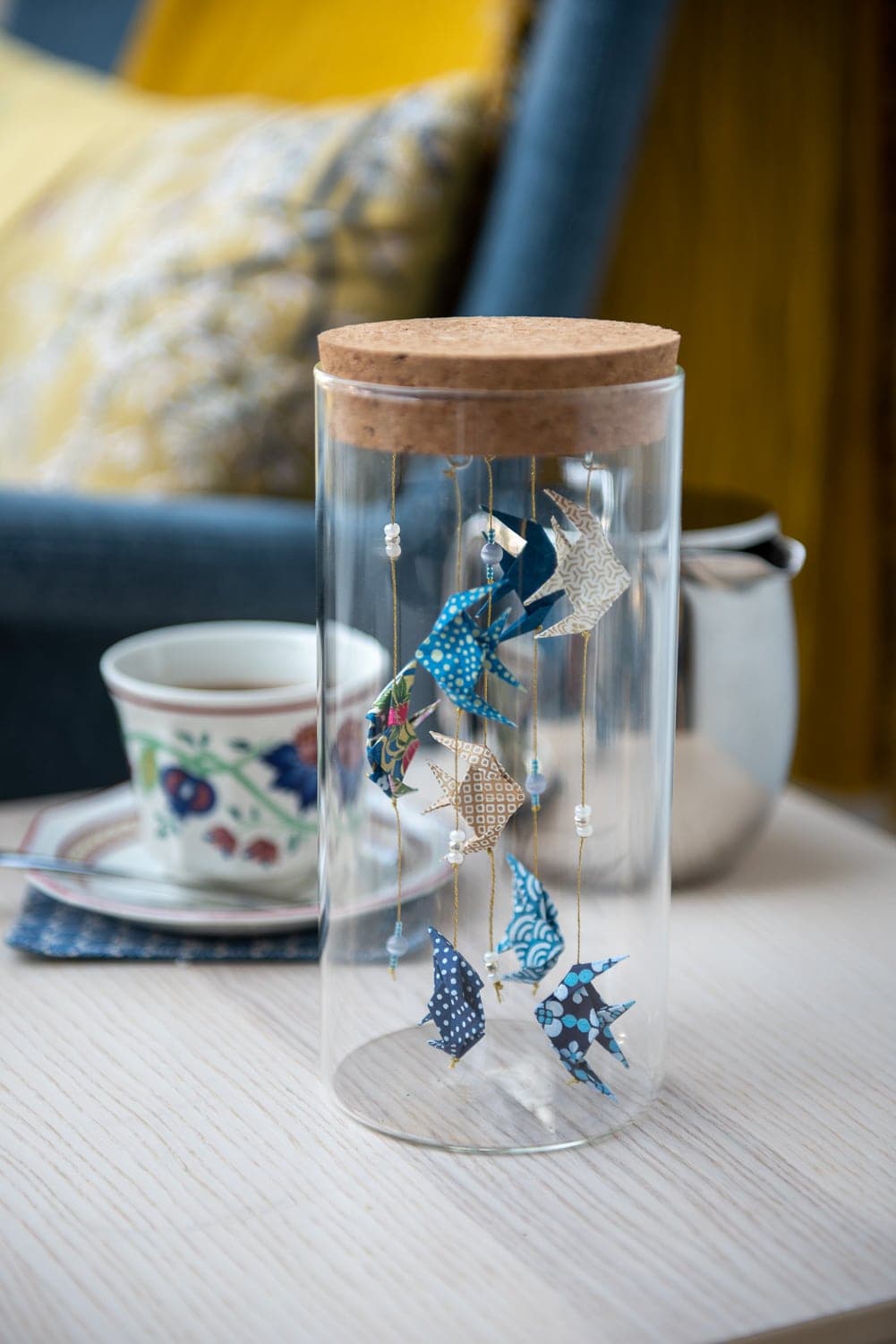 Poissons en origami washi bleu suspendus dans un bocal en verre, sur une table.