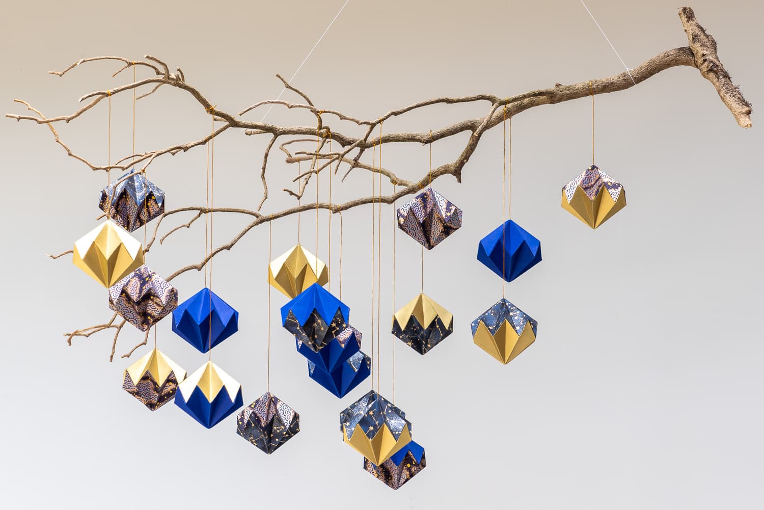 Pierres précieuses en origami washi bleu, blanc et doré, suspendues à une branche.