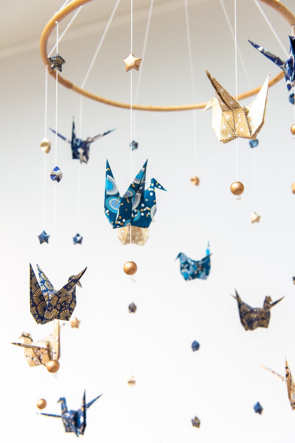 Mobile de grues en origami washi bleu et doré, suspendues à un cerceau en bois.