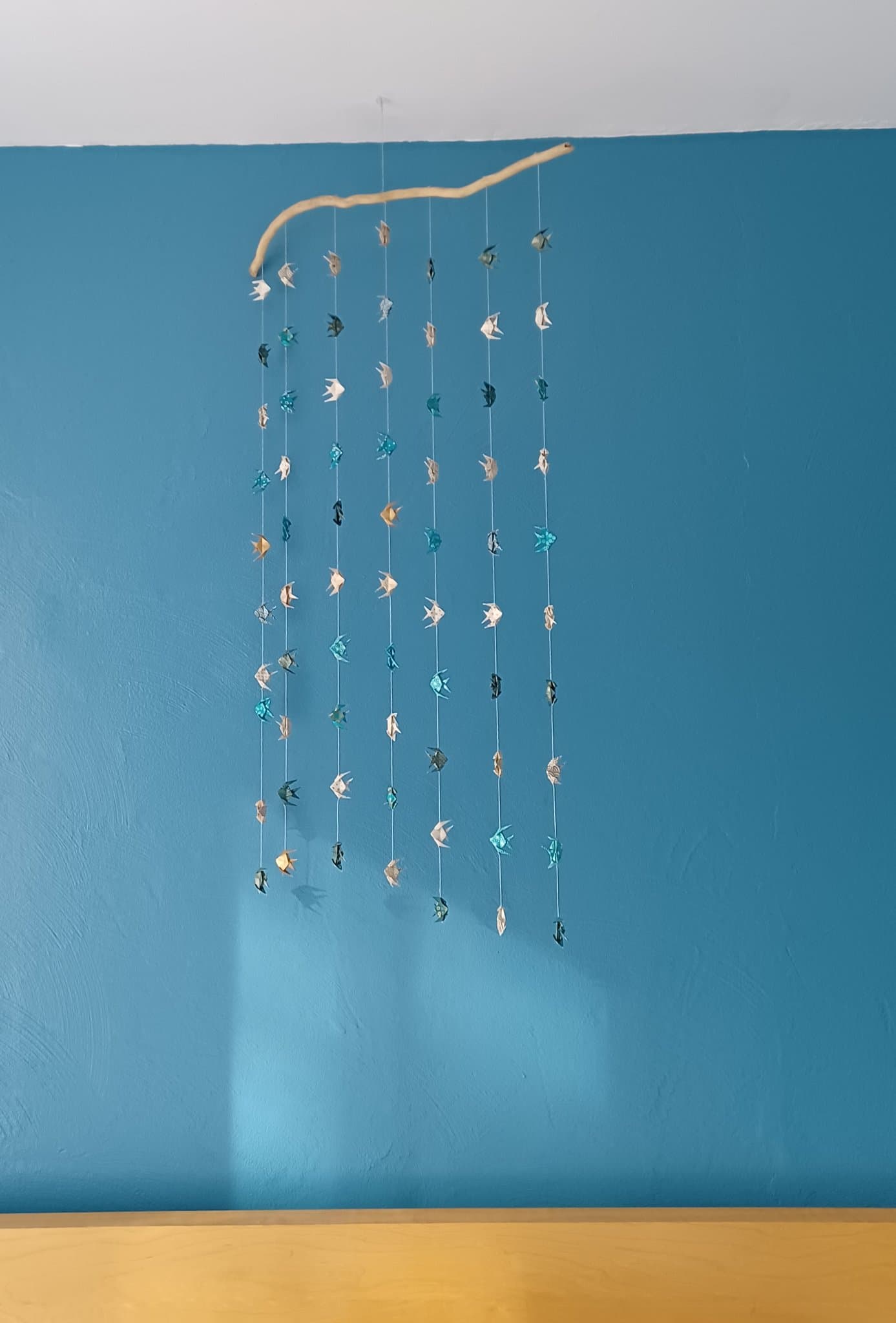 Rangées de petits poissons en origami washi suspendus le long d'un mur bleu.