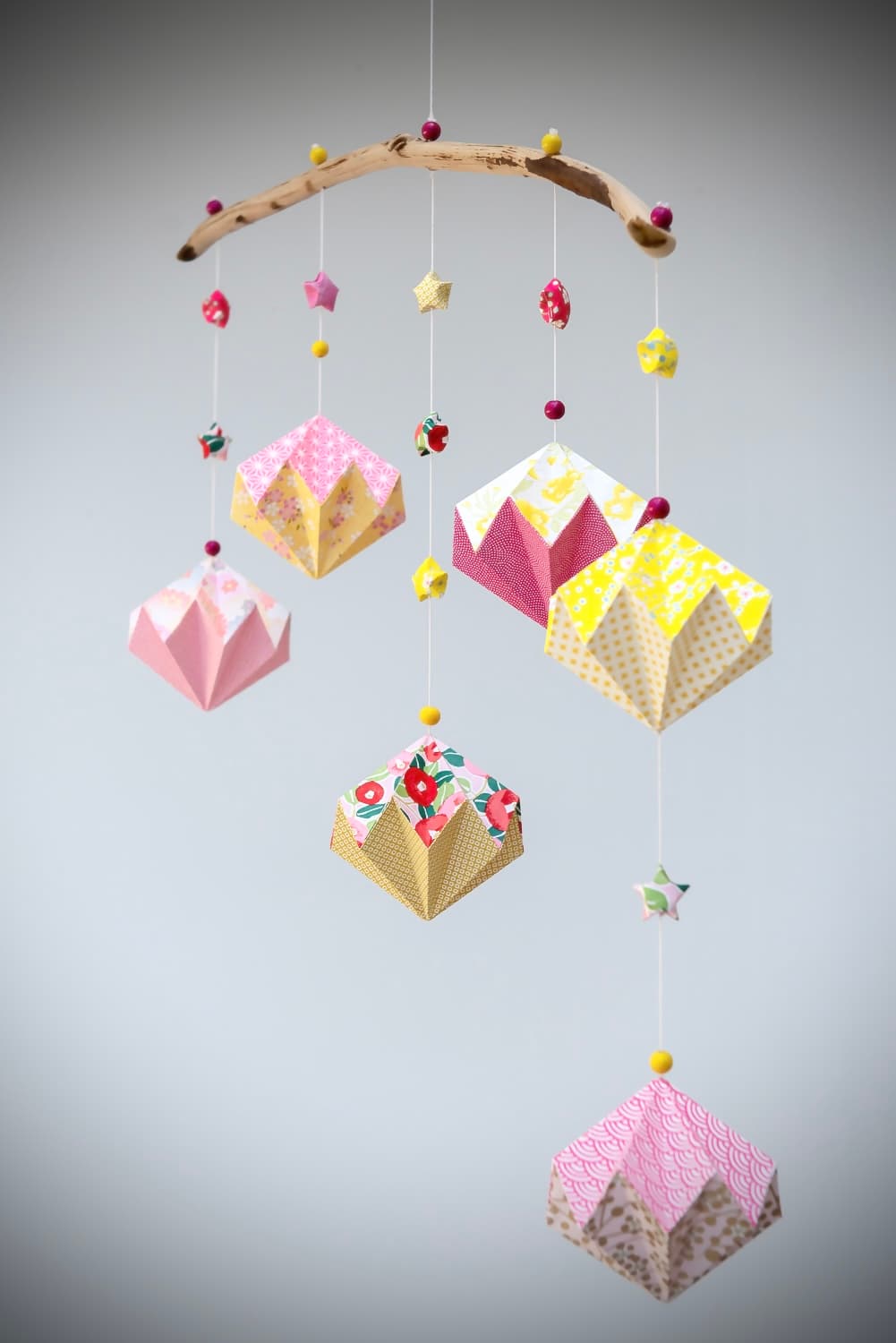 Pierres précieuses en origami washi rose, jaune et blanc, suspendues à une branche.
