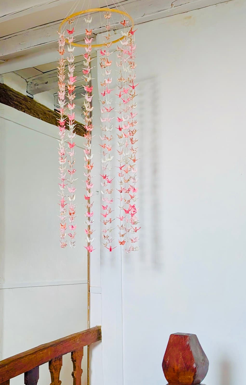 Guirlandes de grues en origami washi rose et blanc, suspendues dans une cage d'escalier.