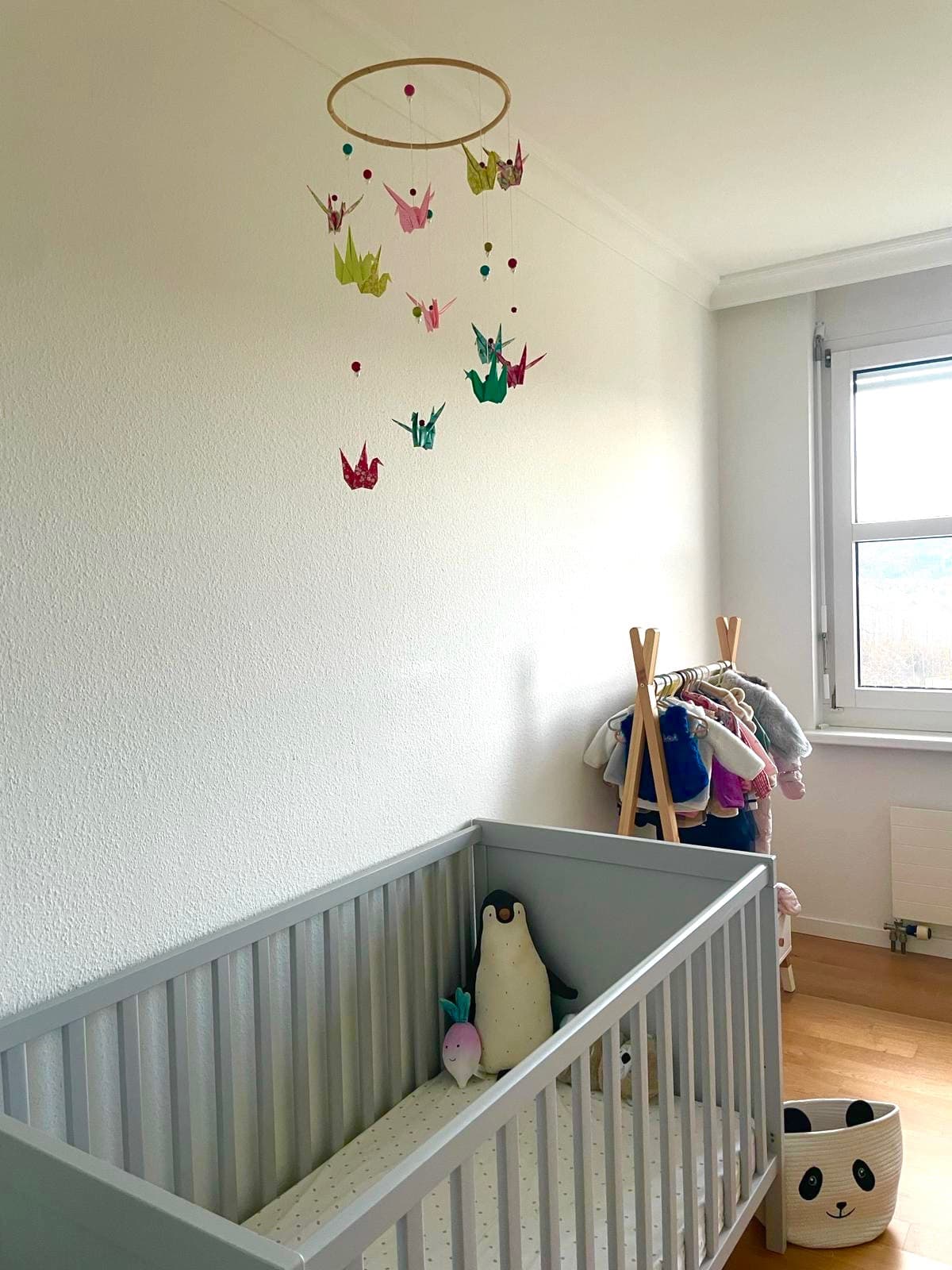 Mobile de grues en origami washi multicolore suspendu au-dessus d'un lit à barreaux.