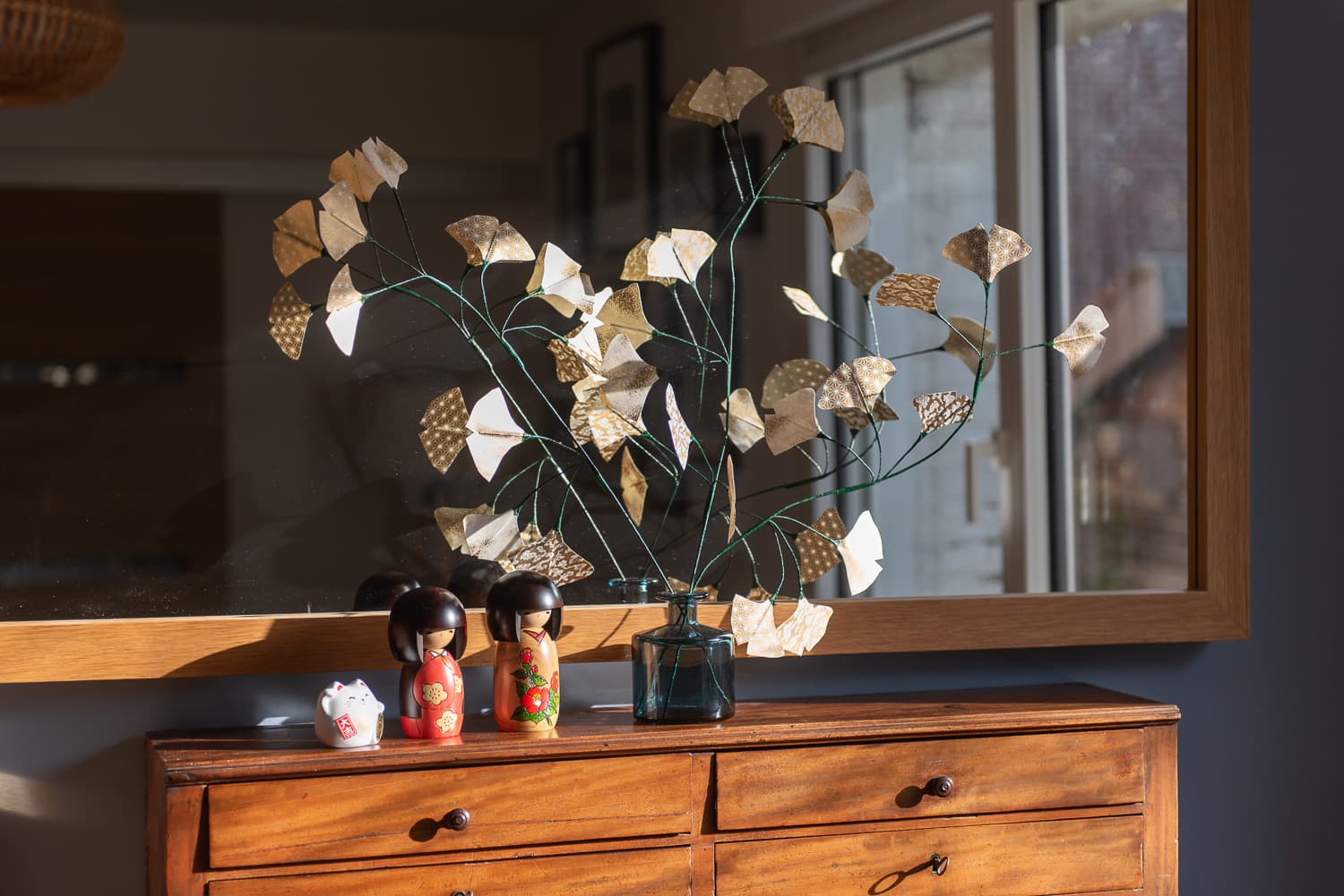 Feuillage en papier washi dans un vase, posé sur un meuble ancien avec des figurines japonaises